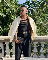 Person wearing a cream jacket over a black outfit with sunglasses, standing outdoors.