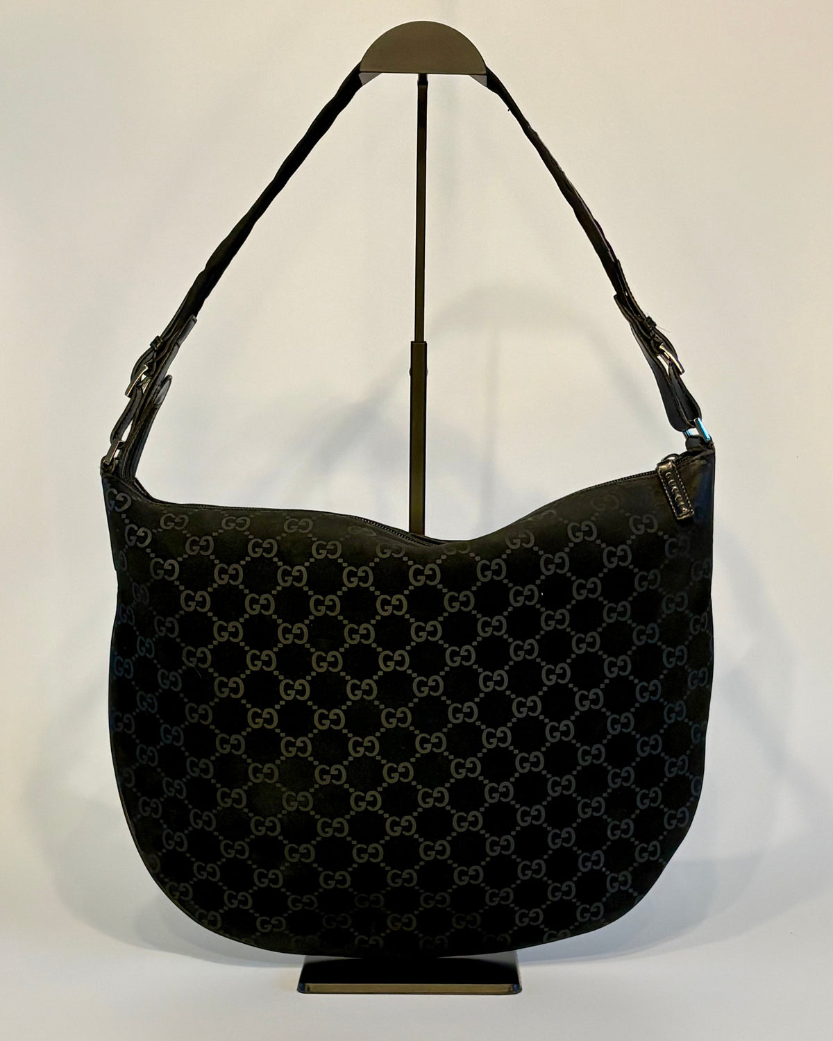 Black vintage Gucci suede shoulder bag displayed upright on a stand, showing its soft GG-patterned surface.