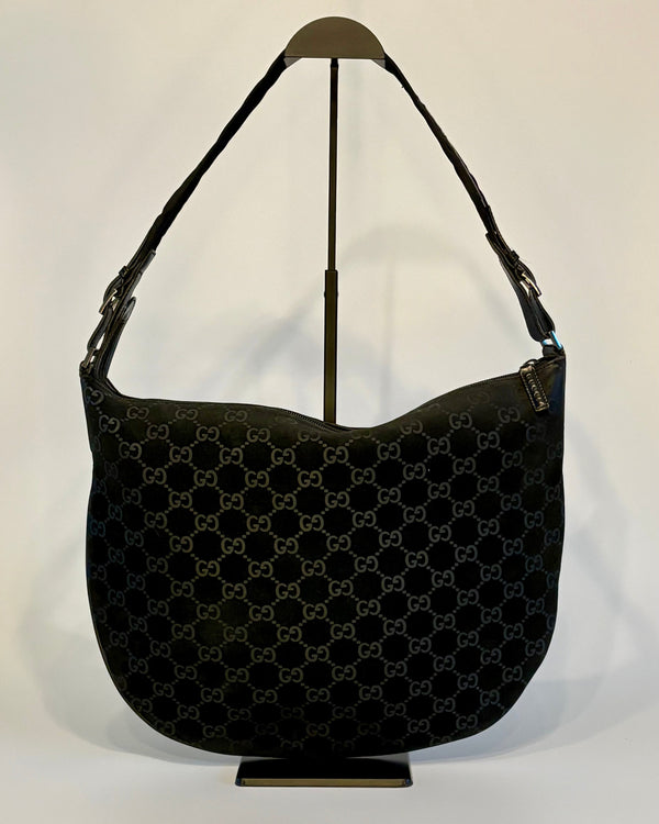 Black vintage Gucci suede shoulder bag displayed upright on a stand, showing its soft GG-patterned surface.