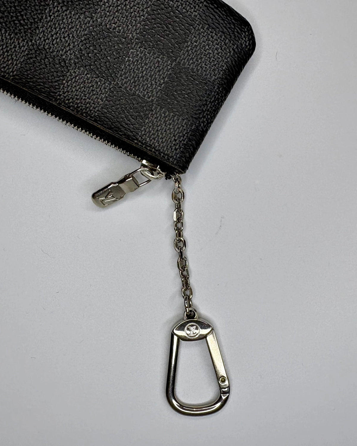 Black zippered pouch with a metal keychain on a light gray background