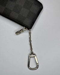 Black zippered pouch with a metal keychain on a light gray background