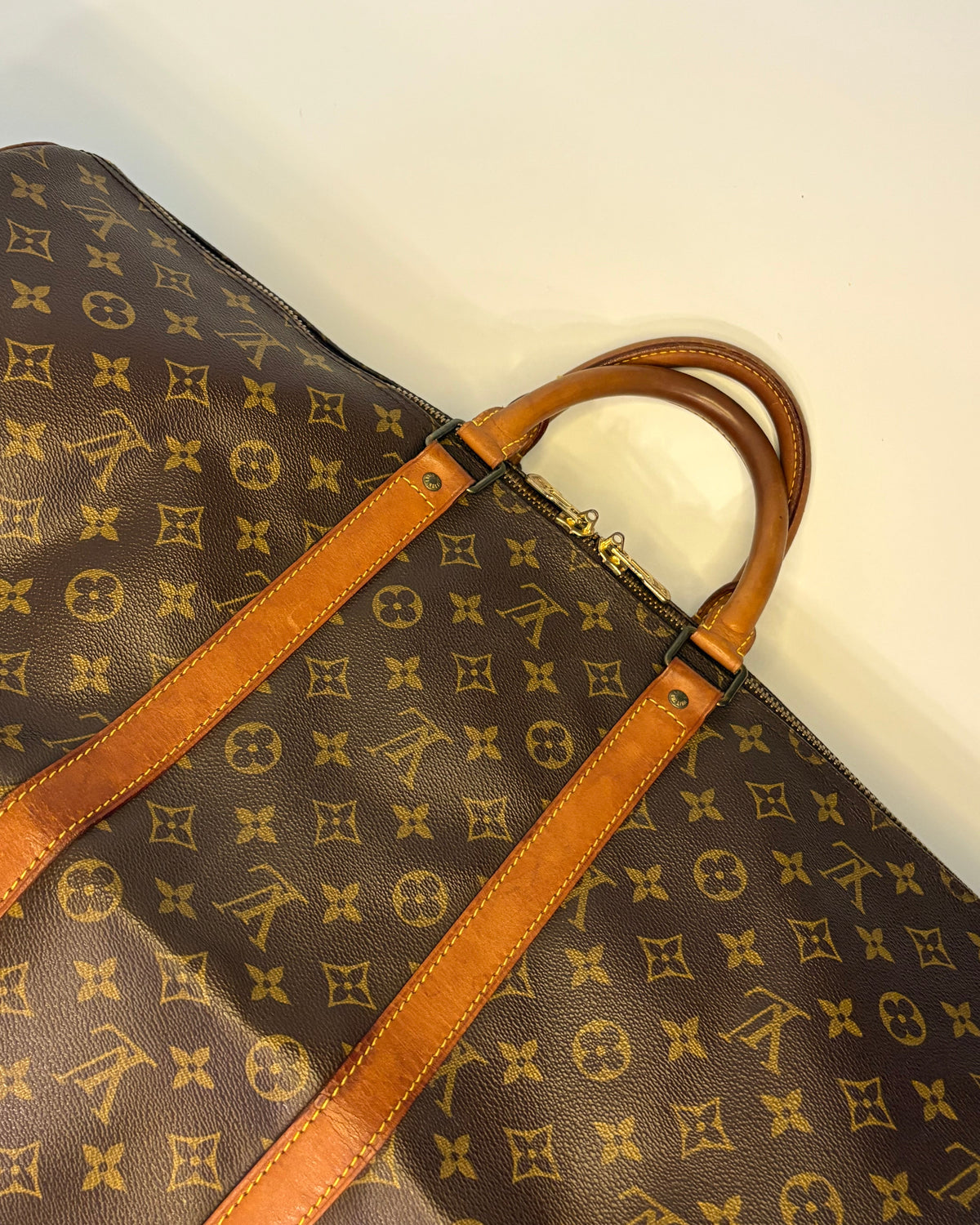 Close-up of the Louis Vuitton Keepall 55 showing the leather trim, yellow stitching and monogram canvas with aged patina.