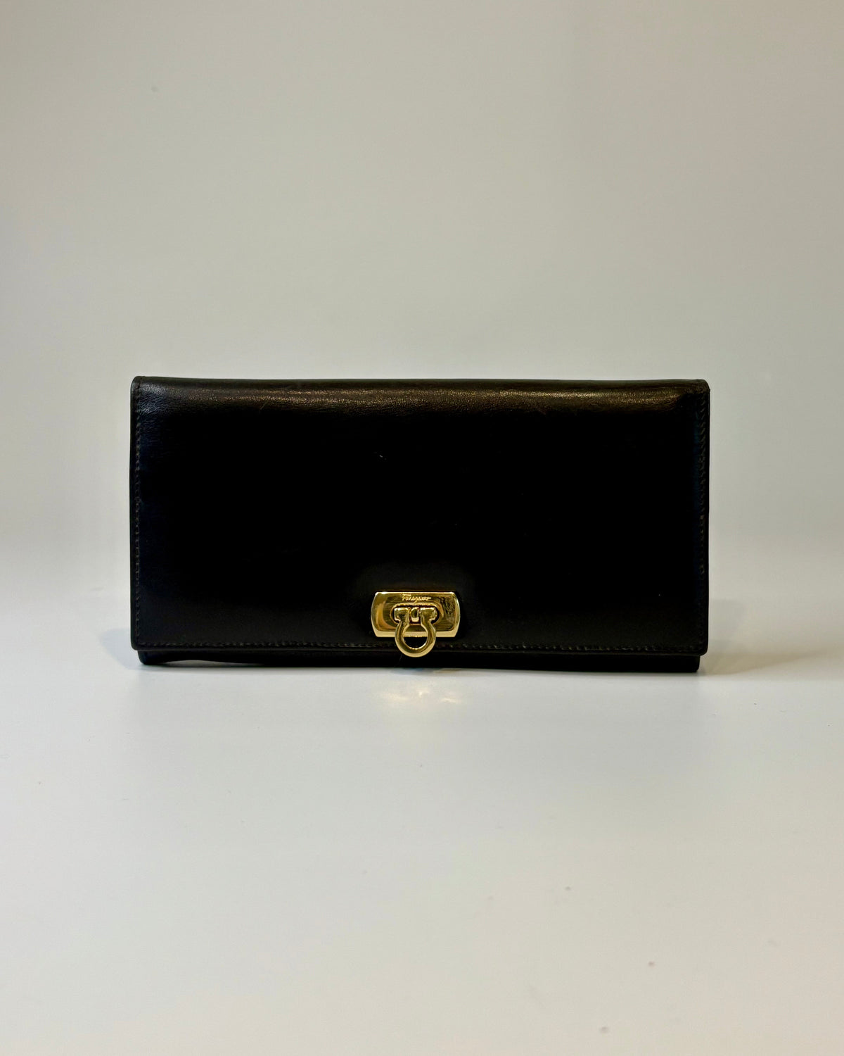 Black Salvatore Ferragamo leather wallet with gold Gancini clasp, displayed closed on a clean light background