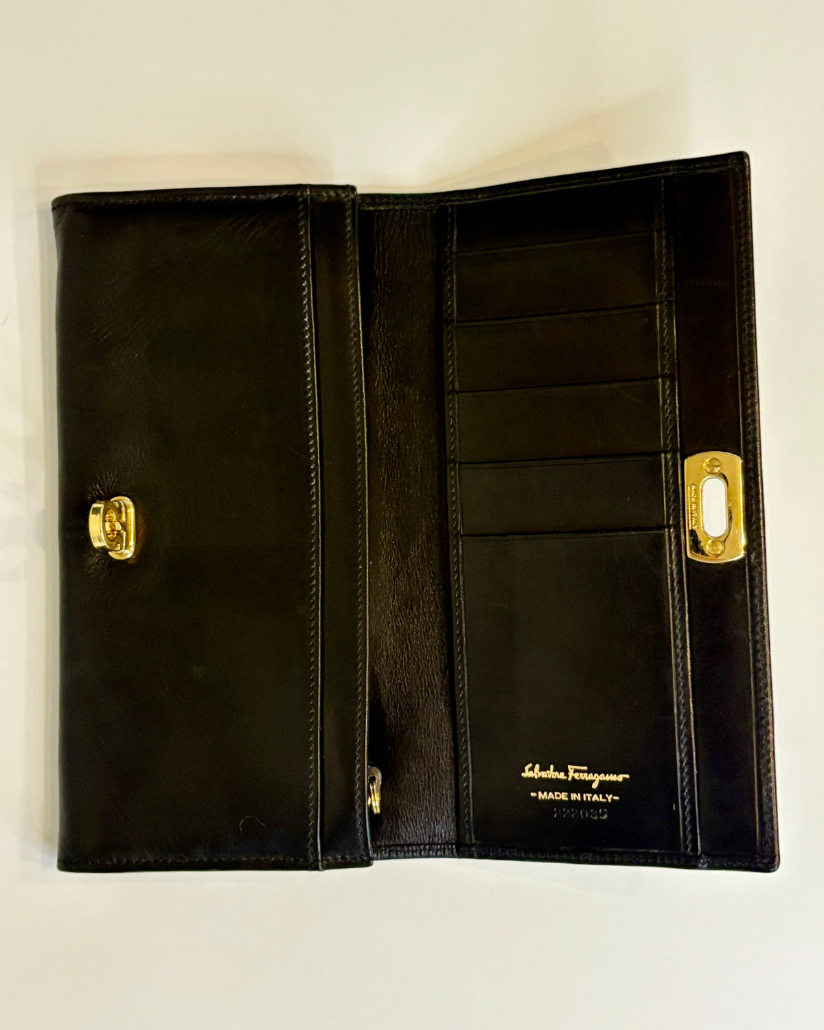 Black Salvatore Ferragamo leather wallet with gold Gancini clasp, displayed closed on a clean light background