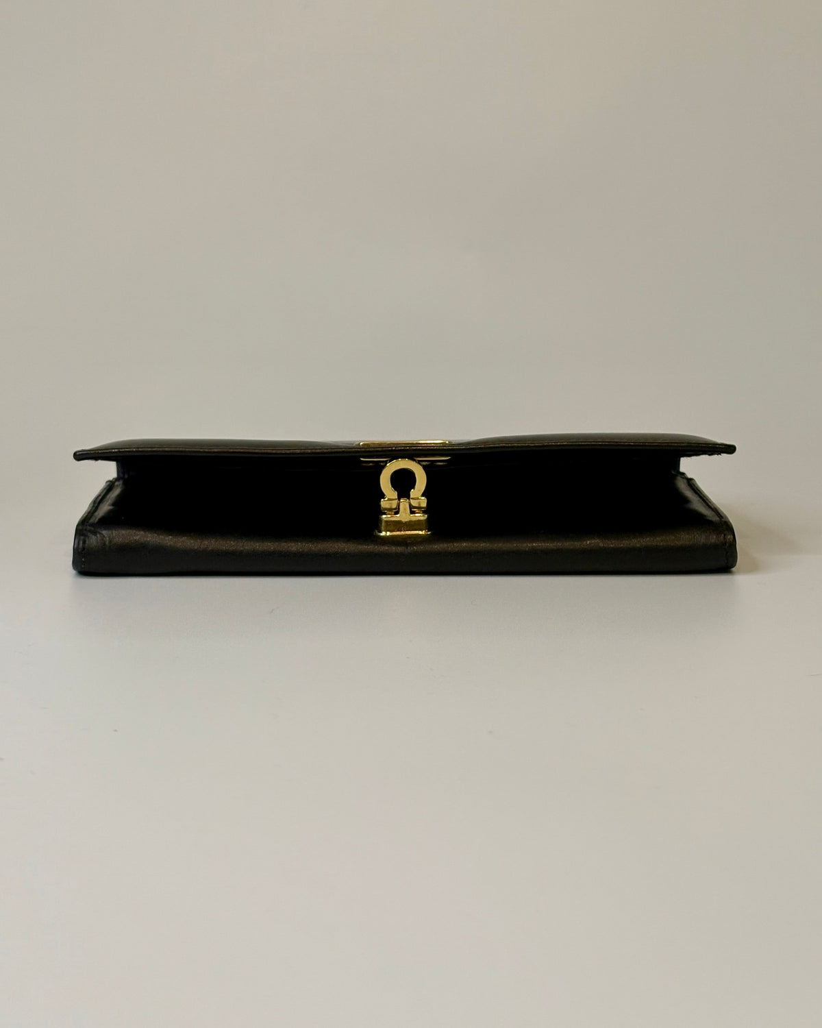 Black Salvatore Ferragamo leather wallet with gold Gancini clasp, displayed closed on a clean light background