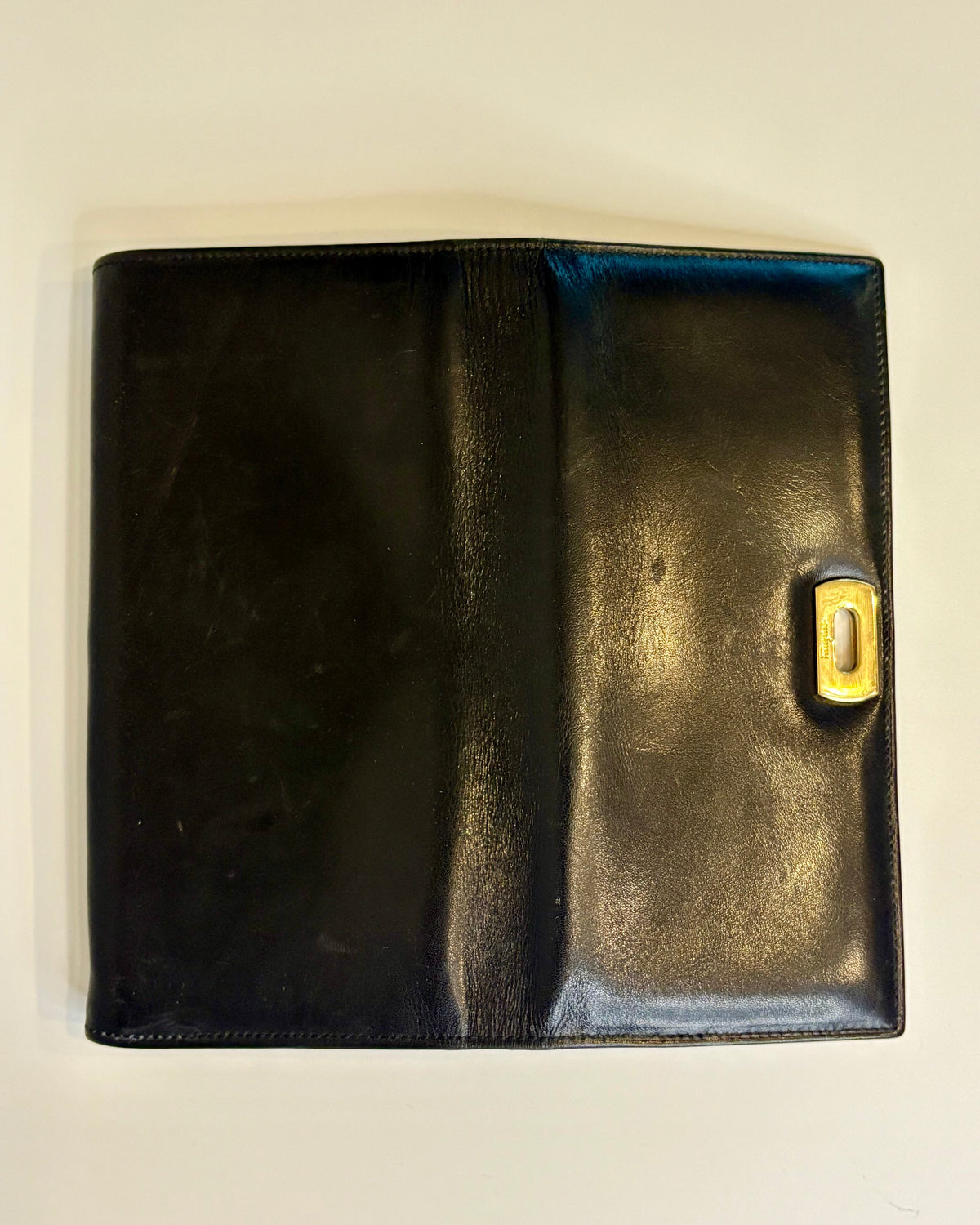 Black Salvatore Ferragamo leather wallet with gold Gancini clasp, displayed closed on a clean light background
