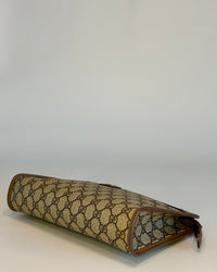 Side-angle photo of the Gucci GG Supreme pouch showing the slim silhouette and structured monogram canvas.

