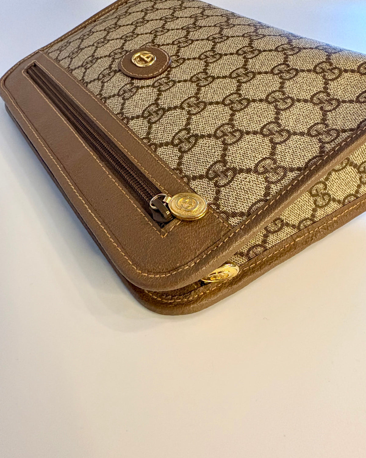 Close-up of the Gucci pouch showing the GG Supreme canvas, leather border and gold zipper detail.