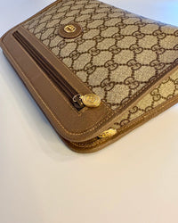 Close-up of the Gucci pouch showing the GG Supreme canvas, leather border and gold zipper detail.